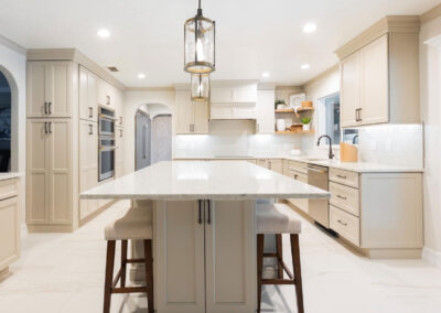 Modern beige kitchen with shaker cabinets, large island, quartz countertops, and built-in appliances.