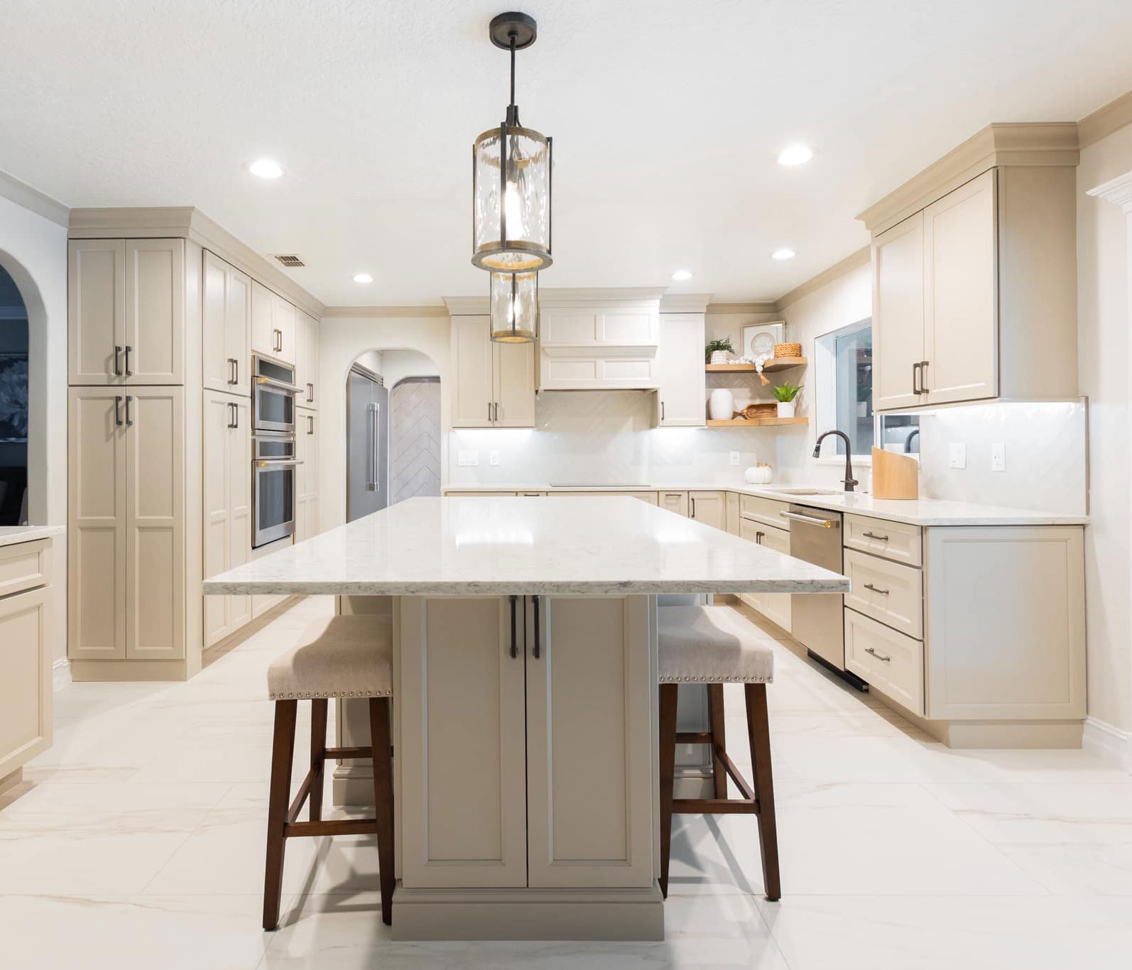 Modern beige kitchen with shaker cabinets, large island, quartz countertops, and built-in appliances.