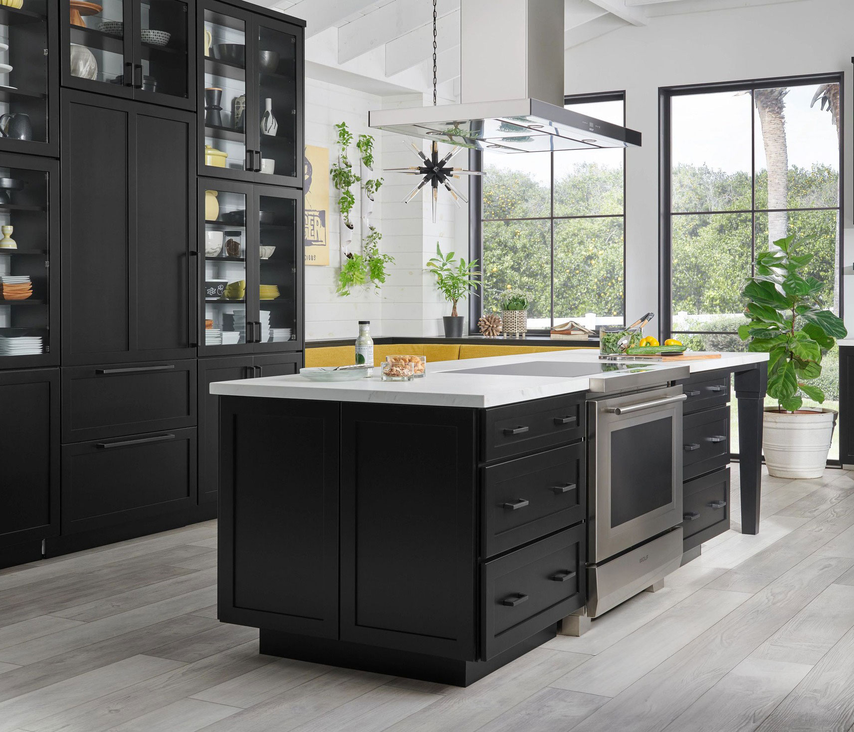 Modern kitchen with black shaker cabinets, large island, glass display uppers, and white quartz countertops.