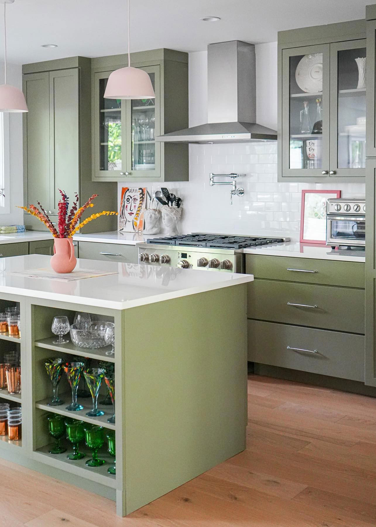 Sage green shaker kitchen cabinets with glass fronts and a matching island with open shelving and white quartz countertops