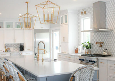 White shaker kitchen cabinets with gold hardware, patterned backsplash, and a large blue island with quartz countertops