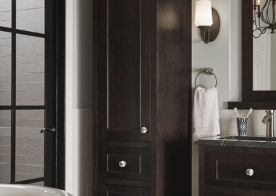 Tall bathroom storage cabinet with white shaker-style doors and brushed metal handles next to a wall with towel hooks.