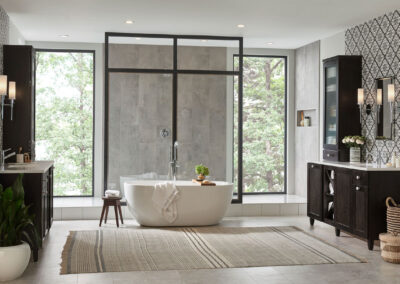 Wide shot of a luxurious bathroom with a white tub, brown cabinets with marble countertops, and a large shower in the back.