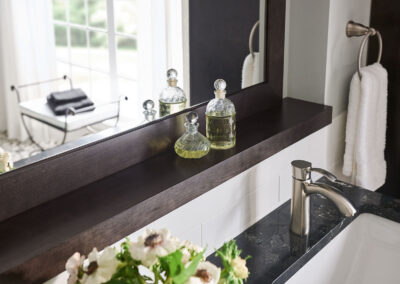 A bathroom mirror with an attached shelf that has perfumes on it.