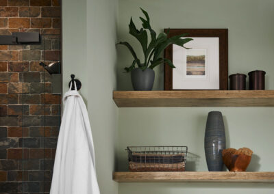 Close up of floating shelves with plants, photos, and decorative items in a green bathroom.