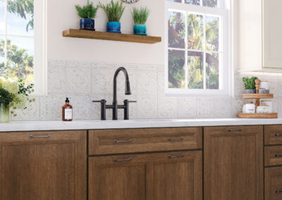 Kitchen sink area with white countertops, brown base cabinets, large window, and black fixtures.