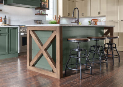 Three adjustable industrial farmhouse kitchen stools with wooden seats tucked under a green kitchen island with wood-trimmed X-end
