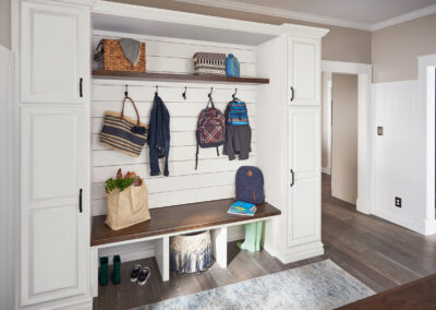 Mudroom with white built-in shelving, upper cubbies, coat hooks, and a wooden bench.
