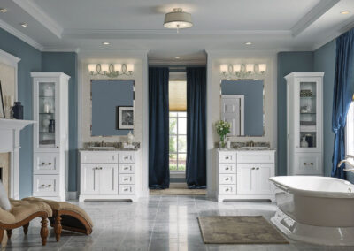 Large blue bathroom with two white vanities with marble countertops, flanked by two tall white cabinets.