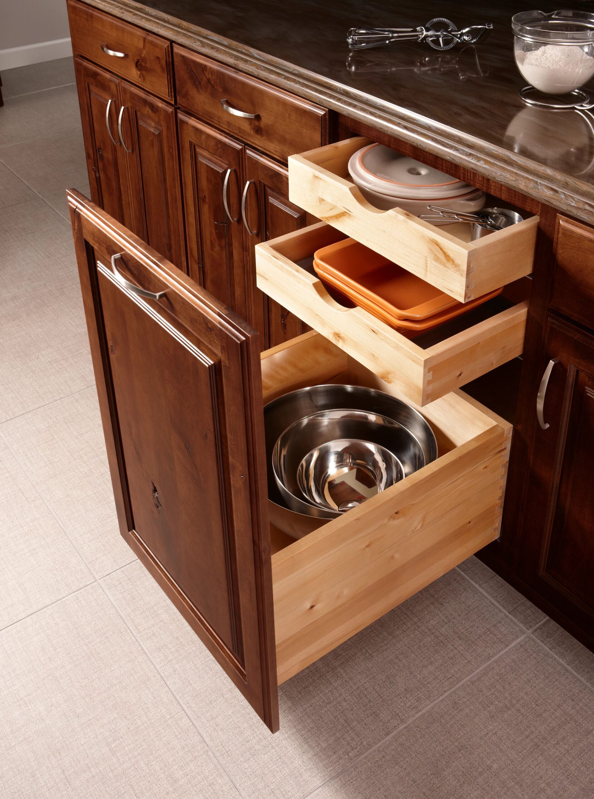 Tilt-out laundry hamper cabinet with a fabric-lined basket holding clothes, set in a dark wood vanity with rolled towels and a potted plant nearby.